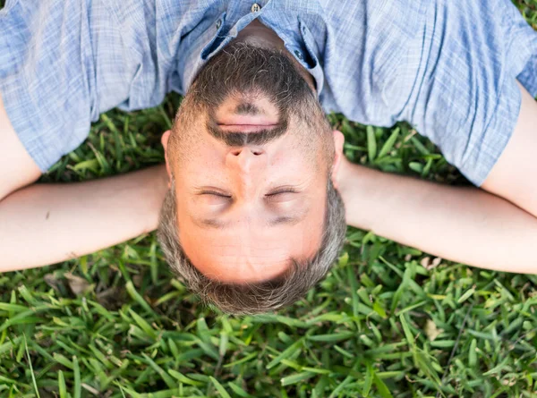 Uomo adulto caucasico sdraiato a testa in giù ritratto sul prato di erba — Foto Stock