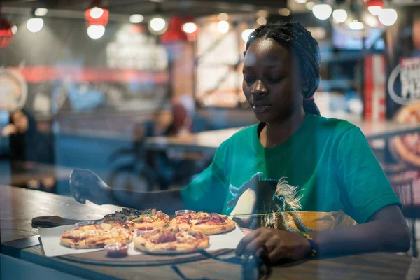Joven mujer negra auténtica sentada con teléfono en la cafetería de la ciudad por la noche Fotos De Stock Sin Royalties Gratis