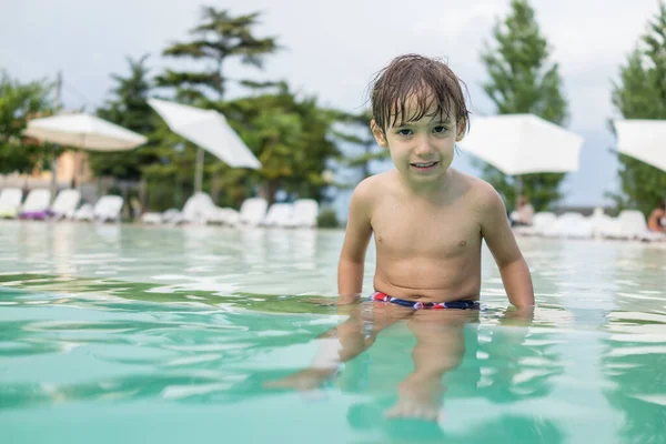 Küçük çocuk yüzme havuzunda su sıçratıyor, eğlenceli aktiviteler yapıyor. — Stok fotoğraf