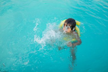 Küçük çocuk yüzme havuzunda su sıçratıyor, eğlenceli aktiviteler yapıyor.