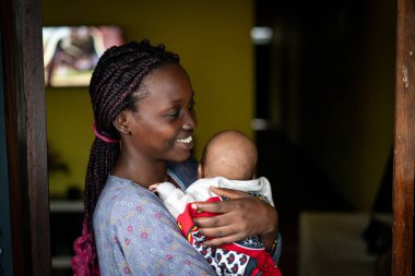 Genç siyah anne kucağında bebek taşıyor.