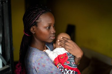 Genç siyah anne kucağında bebek taşıyor.