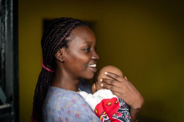 Genç siyah anne kucağında bebek taşıyor.