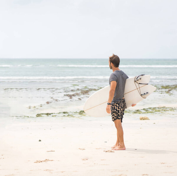 Handsome male surfer with his board on ocean beach