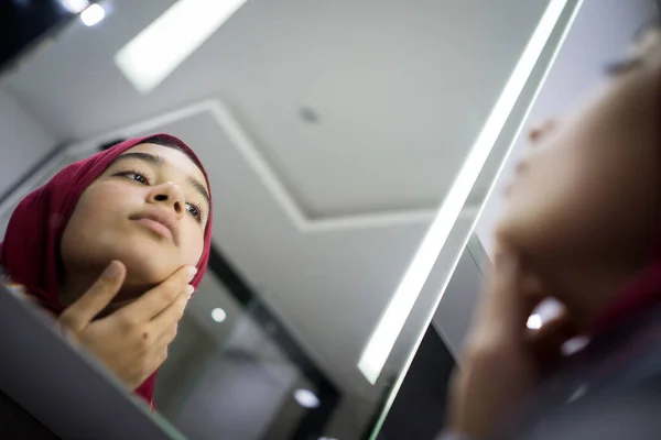 Muslim gadis cantik melihat ke cermin memeriksa kulit wajah — Stok Foto