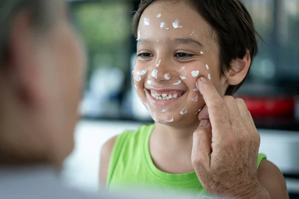 Abuela y niño pequeño poniendo crema de protección en la cara —  Fotos de Stock