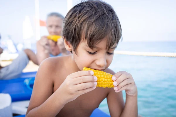 해변 부두에 앉아 옥수수를 먹고 있는 소년 — 스톡 사진
