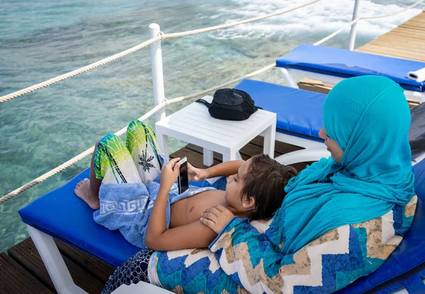 Arab anya és fia ül és élvezi a strand móló — Stock Fotó