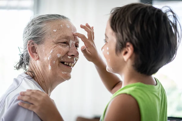 Бабушка и маленький мальчик надевают крем на лицо — стоковое фото