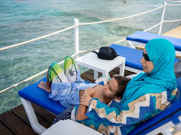 Arabic mother and son sitting and enjoying on beach pier Stock Picture
