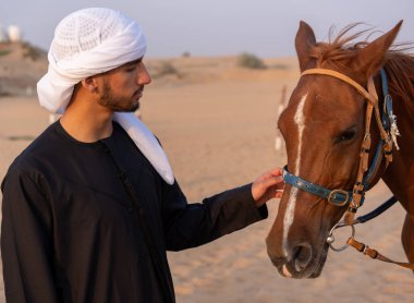 Geleneksel giysiler giymiş bir Arap çölün ortasında at okşuyor. Yüksek kalite fotoğraf