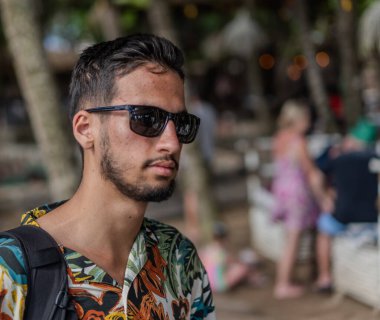 Tropikal tişörtlü bir adam elinde pipetle içki tutarken gülümsüyor. İçki bir limonatadır ve adamın hoşuna gider.