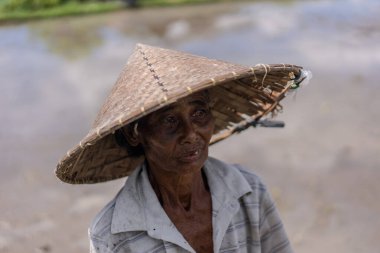 Hasır şapkalı ve beyaz gömlekli bir kadın. Yüzünde ciddi bir ifade var.