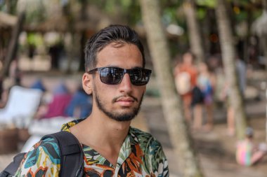 Tropikal tişörtlü bir adam elinde pipetle içki tutarken gülümsüyor. İçki bir limonatadır ve adamın hoşuna gider.