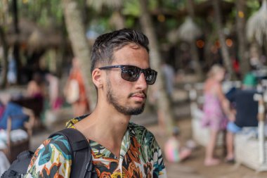 Tropikal tişörtlü bir adam elinde pipetle içki tutarken gülümsüyor. İçki bir limonatadır ve adamın hoşuna gider.