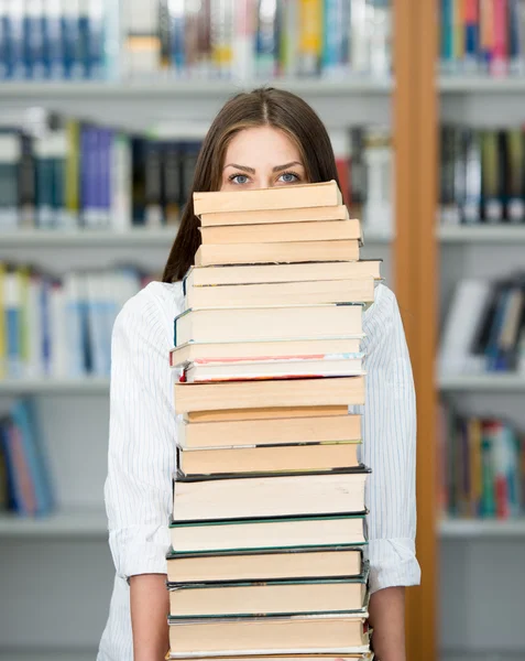 Jovem feliz na biblioteca da faculdade segurando pilha de livros — Fotografia de Stock