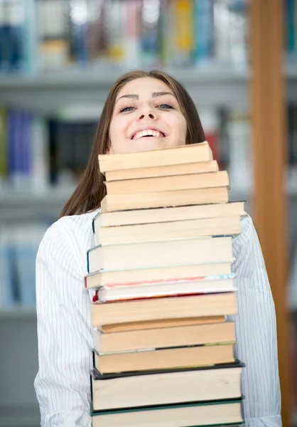 Jovem feliz na biblioteca da faculdade segurando pilha de livros — Fotografia de Stock