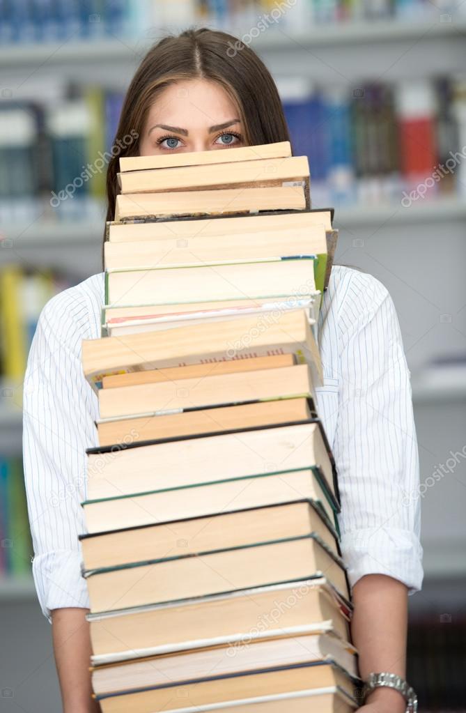 Happy young girl at college library holding stack of books