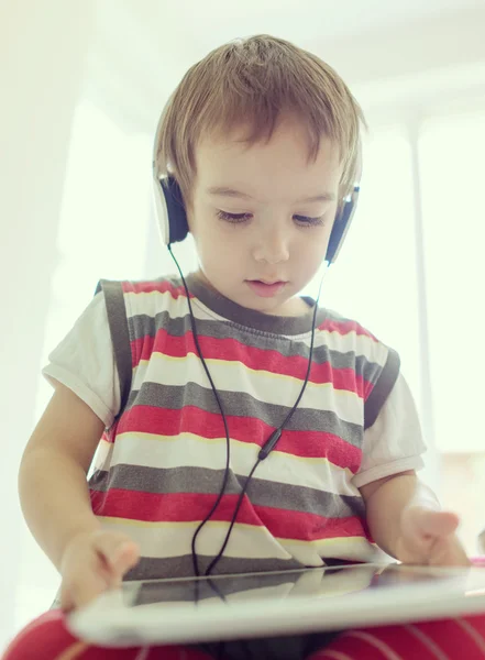 Adorable niño pequeño en casa con tableta y auriculares —  Fotos de Stock