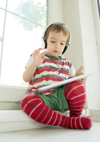 Lindo niño pequeño usando tableta y auriculares —  Fotos de Stock