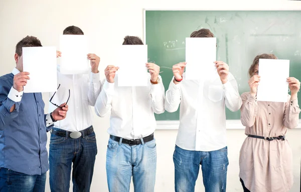 Estudantes segurando folhas de papel em branco na frente das cabeças — Fotografia de Stock