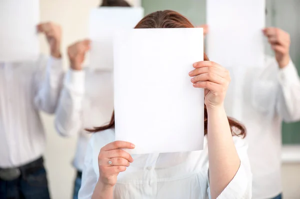 Estudantes segurando folhas de papel em branco na frente das cabeças — Fotografia de Stock