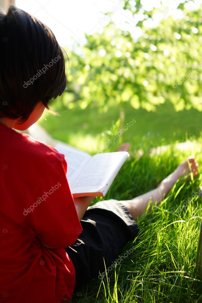 Child reading a book on meadow