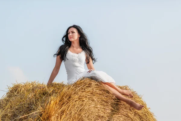 Beautiful brunette woman sitting on hay bale — Stock Photo, Image