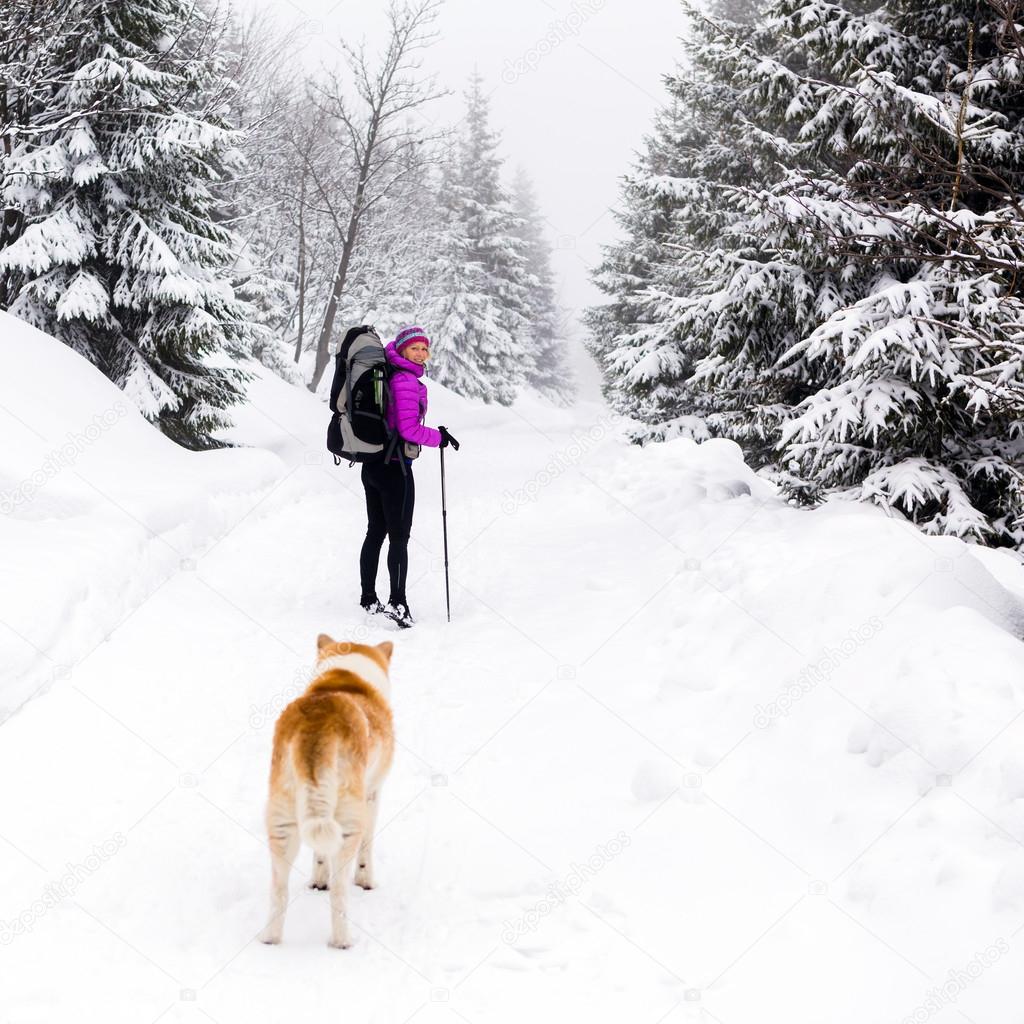 Happy woman walking in winter woods with dog