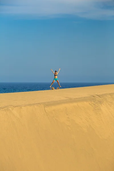 Mujer con los brazos en alto saltando sobre las dunas del desierto de arena — Foto de Stock