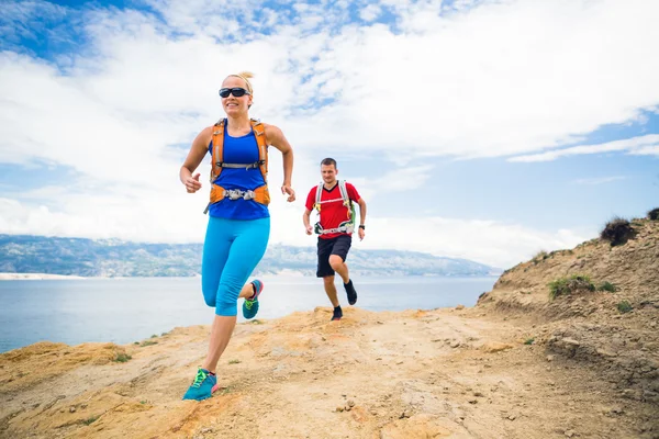 Couple runners running with backpacks on rocku trail at seaside — Stock Photo, Image