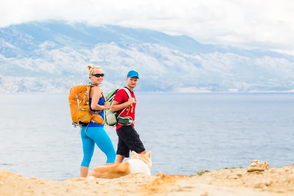Пара туристов гуляют с собакой на берегу моря и в горах — стоковое фото