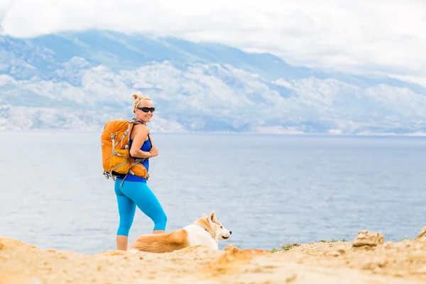 Caminhadas de mulher feliz andando com cão na trilha à beira-mar — Fotografia de Stock