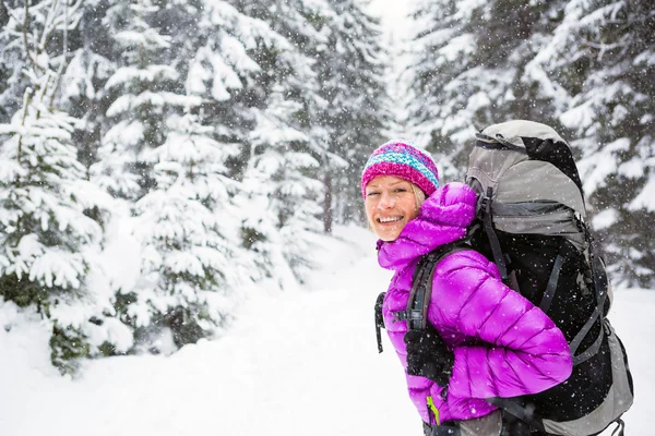 Happy woman walking in winter forest with backpack — Stock Photo, Image