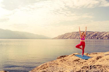 Woman in yoga tree pose meditating at the sea and mountains