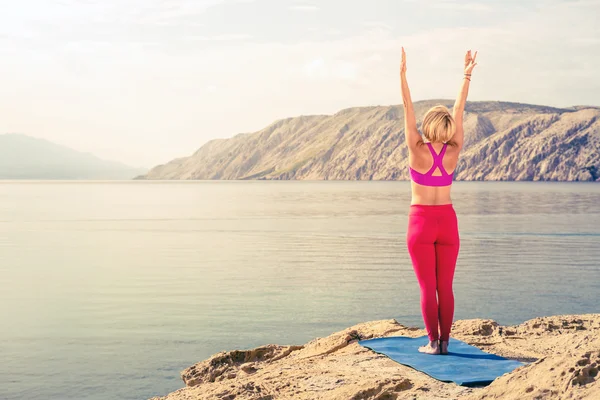 Woman meditating in yoga tree pose at the sea and mountains — ストック写真