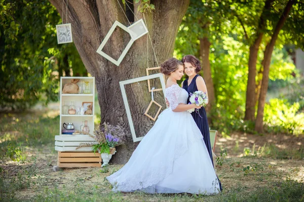 Schöne Braut mit Brautjungfer im Garten — Stockfoto