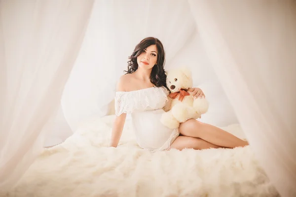 Mulher grávida com urso de brinquedo na cama — Fotografia de Stock