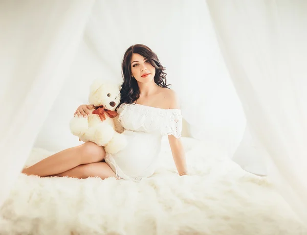 Беременная женщина с игрушечным медведем на кровати — стоковое фото