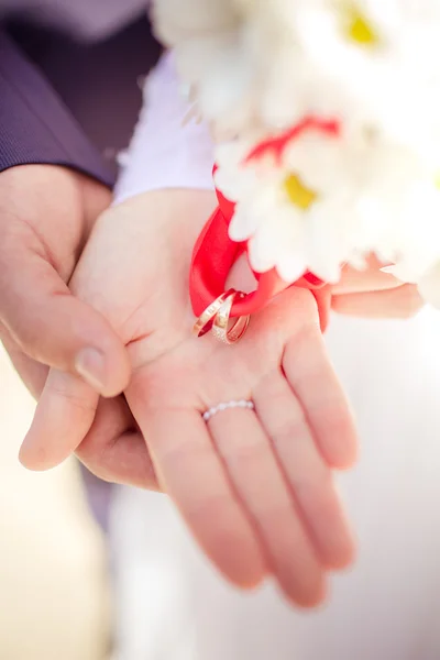 Anéis de casamento em fita vermelha nas mãos — Fotografia de Stock