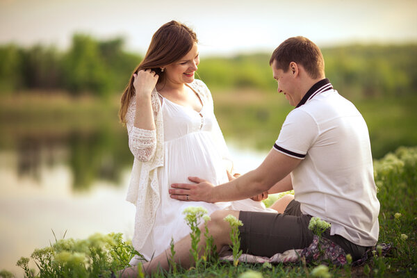 Beautiful pregnant woman with her husband in green meadow