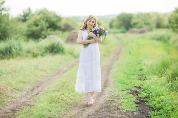 Beautiful pregnant woman with a bouquet of flowers in nature