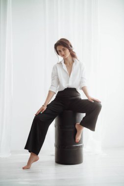 Beyaz gömlekli genç bir kadın stüdyoda poz veriyor.