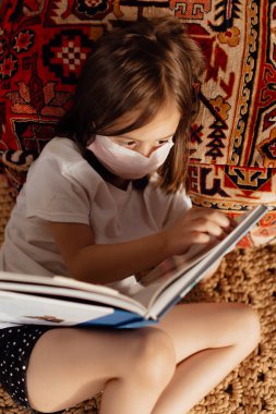  Yüz maskeli küçük kız kendini izole etme konusunda kendini eğitiyor. Koronavirüs salgınları nedeniyle karantina sırasında aile desteği.