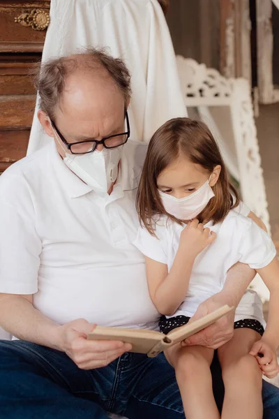 Little granddaughter in a face mask hugs and wants to protect grandfather from an epidemic. Family support during quarantine isolation due to outbreaks of coronavirus. Elderly at risk