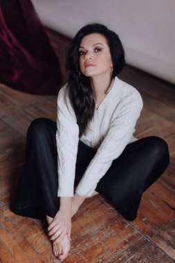 Beyaz kazaklı güzel esmer kadın yerde poz veriyor.