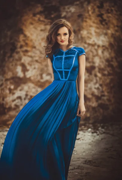Meisje in lange blauwe jurk op een kust — Stockfoto