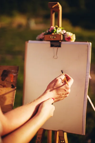 Male and female hands with paintbrushes and easel — Stock Photo, Image