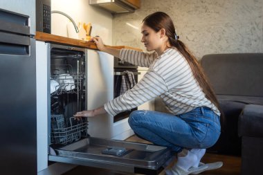 Kadın bulaşık makinesini açıyor. Zaman kazandıran teknoloji. Dahili bulaşık makinesini aç. Entegre aletleri olan beyaz mutfak. Bulaşık makinesinde temiz tabaklar ve bulaşıklar