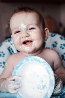 Bebek sandalyesinde oturup yoğurt tabağıyla oynadığı için çok mutlu..
